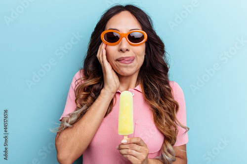 Young latin woman holding an ice cream isolated on blue background
