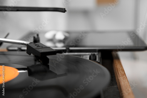 Selective focus on the head of a gramophone moving on a music record. behind it is a tablet computer and white wireless headphones on it.
