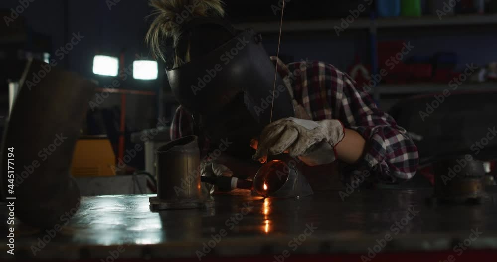 Female mechanic wearing welding helmet welding while sitting at car service station Female mechanic wearing welding helmet welding while sitting at car service station
