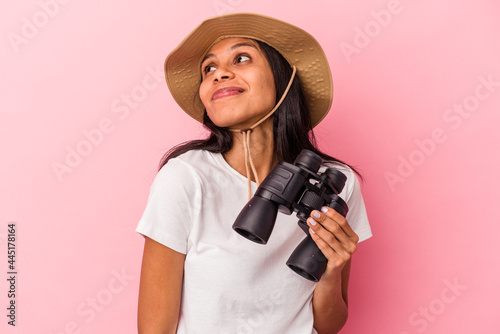 Young latin woman holding binoculars isolated on pink background dreaming of achieving goals and purposes
