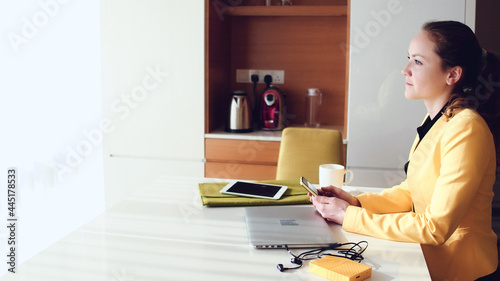 Young beautiful woman wearing a yellow jacket sitting on an office chair while using a laptop. photo