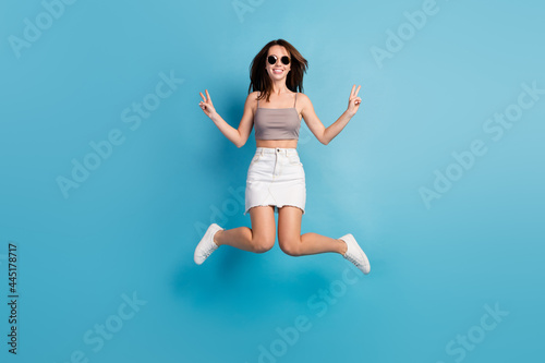 Full size photo of positive nice happy woman jump up v-signs cool hello smile isolated on blue color background