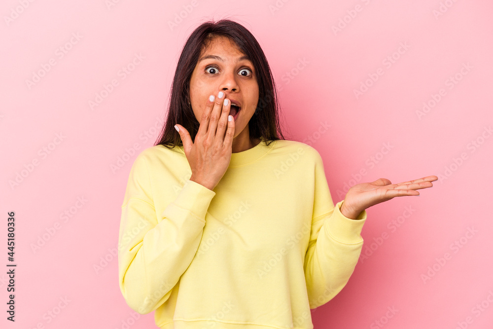 Young latin woman isolated on pink background impressed holding copy space on palm. Young latin woman isolated on pink background impressed holding copy space on palm.