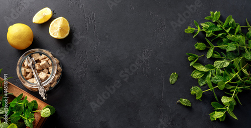 Fresh mint in wooden box on dark concrete background with lemons and cane sugar cubes. Top view of a bunch of mint and mint leaves. Copy space for your design.