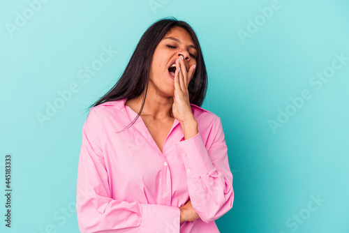 Young latin woman isolated on blue background yawning showing a tired gesture covering mouth with hand.