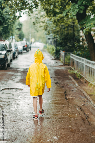 A boy in a yellow raincoat comes out in the rain. child alone walks in the rain. Back view in a bright raincoat. walk in puddles