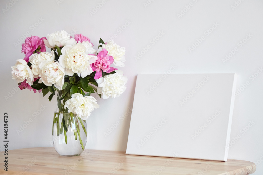 Canvas mockup with pink flowers on wooden table on white wall background Canvas mockup with pink flowers on wooden table on white wall background