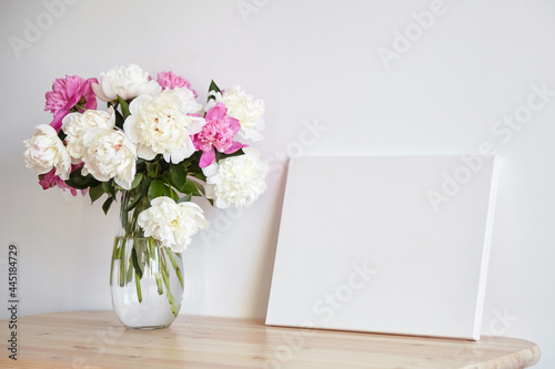 Canvas mockup with pink flowers on wooden table on white wall background