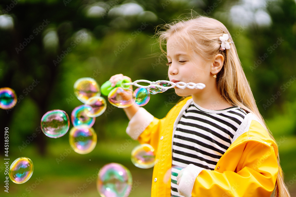 Little adorable girl blowing soap bubbles outdoors in summer park. Happy childhood concept.