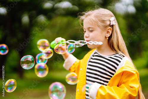 Little adorable girl blowing soap bubbles outdoors in summer park. Happy childhood concept.