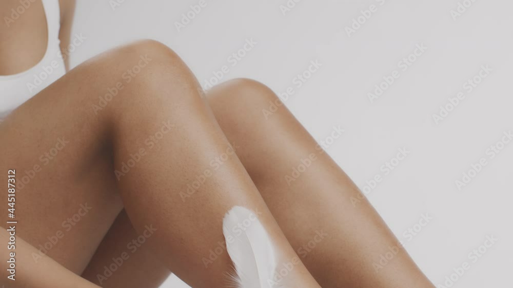 Effective hair removal procedures. Unrecognizable african american woman caressing legs with smooth skin with feather