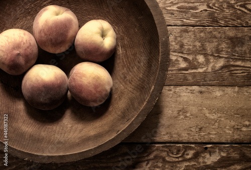 An assortment of fresh peaches in a old hand made wooden bowl on a wooden table.