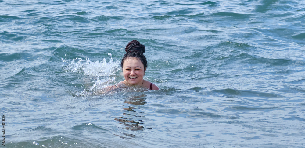A happy young asian woman in a swimsuit, swimming into the sea and smiling.