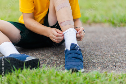 School boy putting on shoes band aids on legs covering scrapes photo
