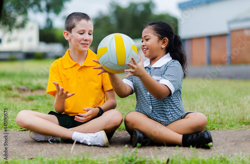 Aussie Boy and girl in playground at primary school throwing ball to each other photo