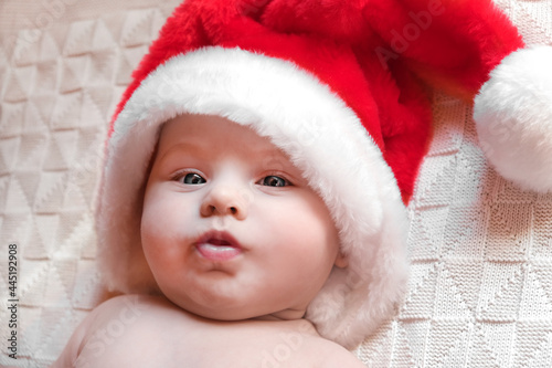 Beautiful little child is celebrating Christmas. New Year's holidays. A child in a Christmas costume. Childhood and people concept - happy Newborn baby in Santa hat over knitted background