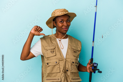 Young african american fisherwoman holding rod isolated on blue background feels proud and self confident, example to follow.
