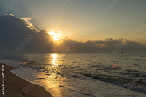 Obraz na płótnie Golden hour, the sun's rays make their way through the clouds above the water su