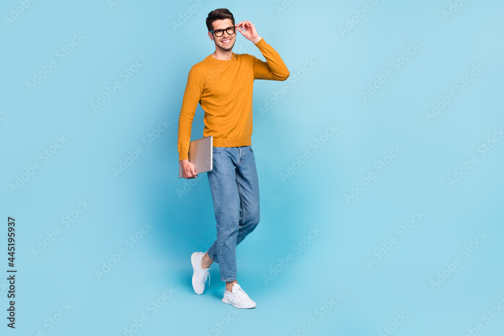 Photo of attractive cute young man wear yellow sweater arm spectacles smiling walking holding modern gadget isolated blue color background