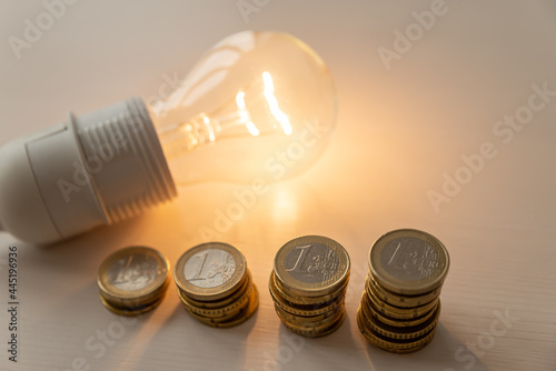 Lit light bulb with coins beside it. Increase in energy tariffs. Efficiency and energy saving. 
