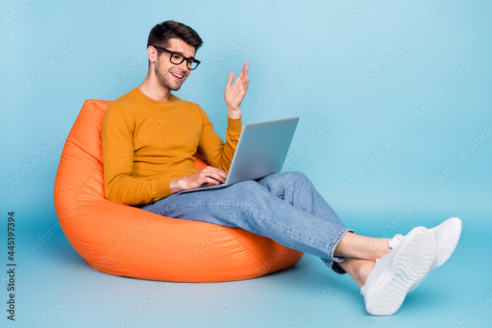 Portrait of attractive cheerful guy sitting in chair using laptop calling contact isolated over bright teal blue color background