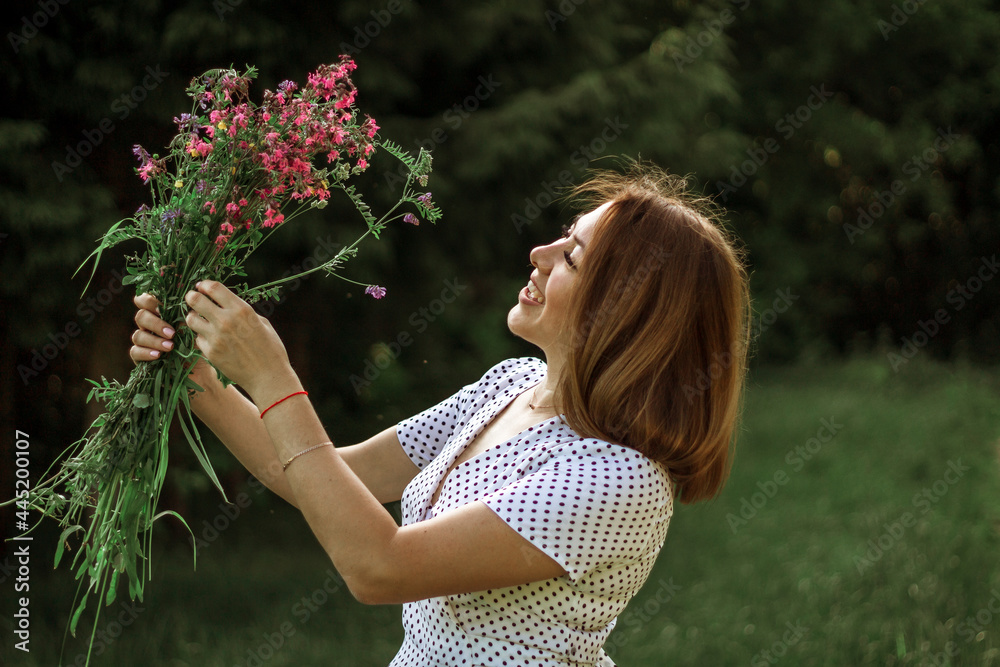 A girl in a white light dress is holding a bouquet of wild flowers over her head and spinning. Copy space, selective focus A girl in a white light dress is holding a bouquet of wild flowers over her head and spinning. Copy space, selective focus