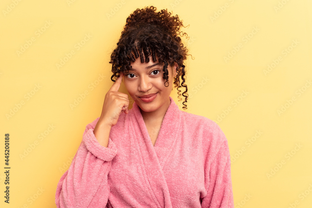 Young mixed race woman wearing a pink bathrobe isolated on pink background pointing temple with finger, thinking, focused on a task. Young mixed race woman wearing a pink bathrobe isolated on pink background pointing temple with finger, thinking, focused on a task.