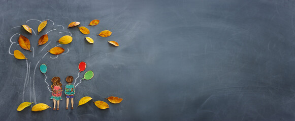 Back to school concept. Top view banner of boy and girl next to tree sketch with autumn dry leaves over classroom blackboard background