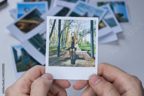 A person holds a polaroid photo in his hands against the background of other photos. Photo in hand close-up. A person looks at a photo from a polaroid.