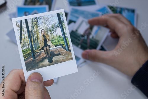 A person holds a polaroid photo in his hands against the background of other photos. Photo in hand close-up. A person looks at a photo from a polaroid.