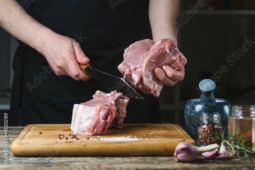 Fototapeta Naklejka Na Ścianę i Meble -  The butcher cuts the pork ribs. Meat with bone on a wooden cutting board. Chef slicing raw meat.