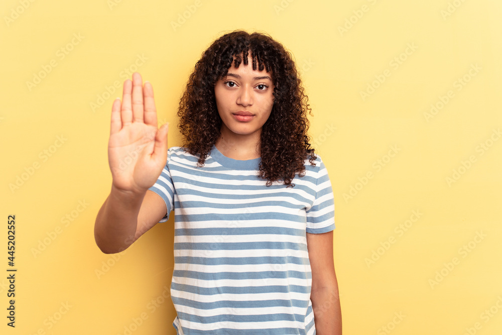Young mixed race woman isolated on yellow background standing with outstretched hand showing stop sign, preventing you. Young mixed race woman isolated on yellow background standing with outstretched hand showing stop sign, preventing you.
