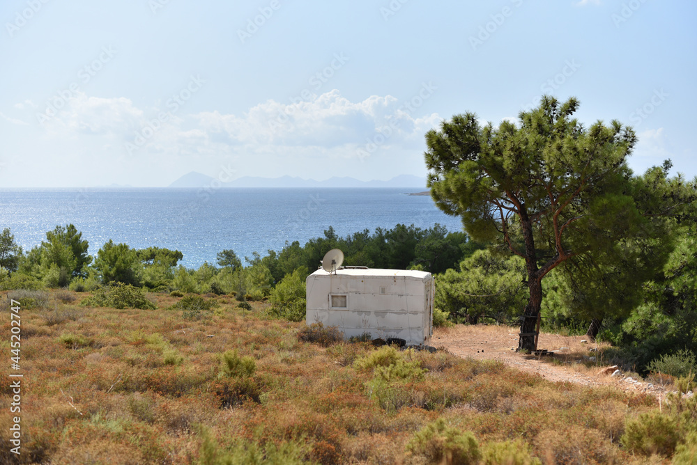 Obraz premium Old shabby fully autonomous caravan with satellite antenna and solar panels on roof - downshifter hermit's dwelling is escaped from city on coast sea. Counterurbanization or deurbanization concept.