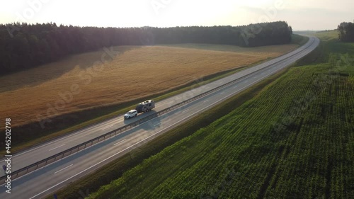 Aerial view of a caravan trailer travelling being towed through the highway. Van with a trailer drives along a wide two-lane road, in the rays of the dawn sun. Camping travel concept. photo