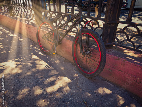 Black bicycle bike single-speed with red wheels parked on the street near old fence © mettus