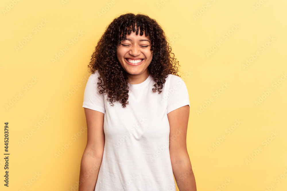 Young mixed race woman isolated on yellow background laughs and closes eyes, feels relaxed and happy. Young mixed race woman isolated on yellow background laughs and closes eyes, feels relaxed and happy.