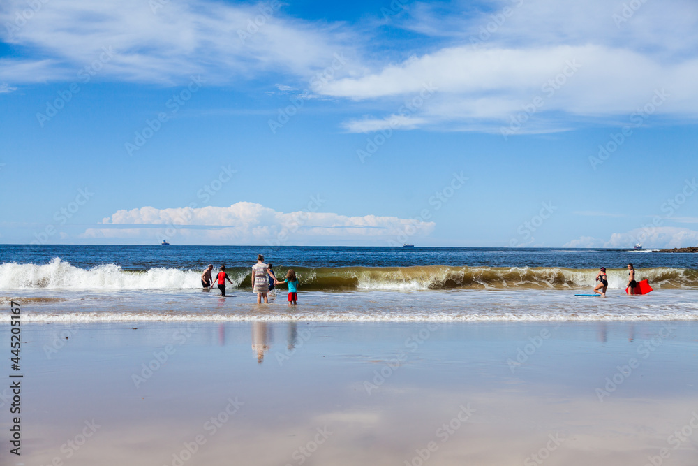 Family and distant people playing on Australian beach on sunlit day Family and distant people playing on Australian beach on sunlit day