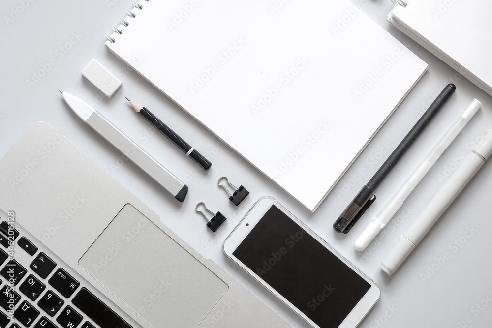 Modern workspace with smartphone, notepad, laptop, pens, on gray background. Monochrome, flat lay. Modern workspace with smartphone, notepad, laptop, pens, on gray background. Monochrome, flat lay.
