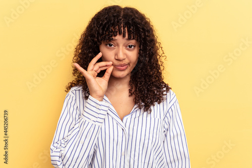 Young mixed race woman isolated on yellow background with fingers on lips keeping a secret.