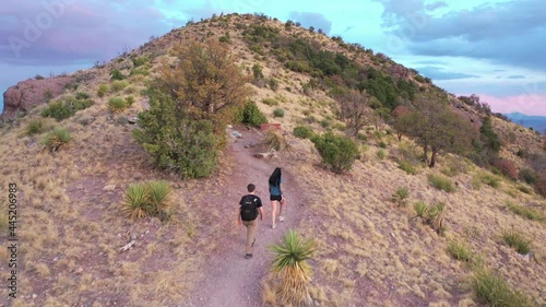 View of two women climbing to the top of a mountain in Arizona with a sunset in the background. Both women are athletic and are walking.