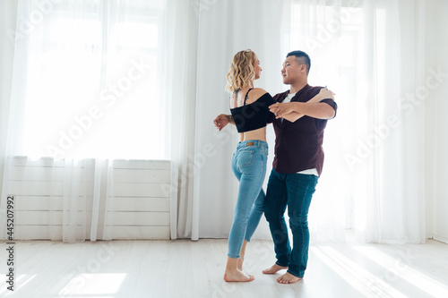 beautiful man and woman dancing together to music in a white room © dmitriisimakov