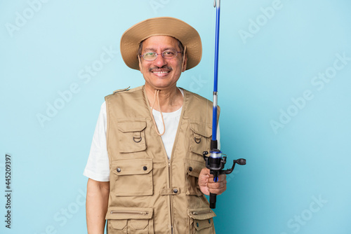 Senior indian fisherman holding rod isolated on blue background happy, smiling and cheerful.