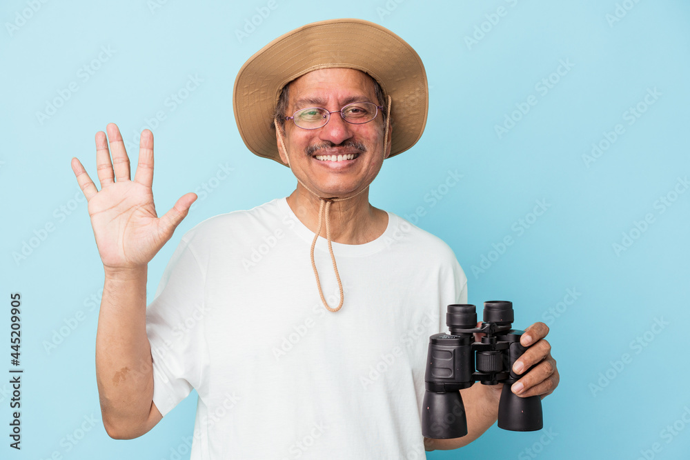 Middle aged indian fisherman holding rod isolated on blue background smiling cheerful showing number five with fingers. Middle aged indian fisherman holding rod isolated on blue background smiling cheerful showing number five with fingers.