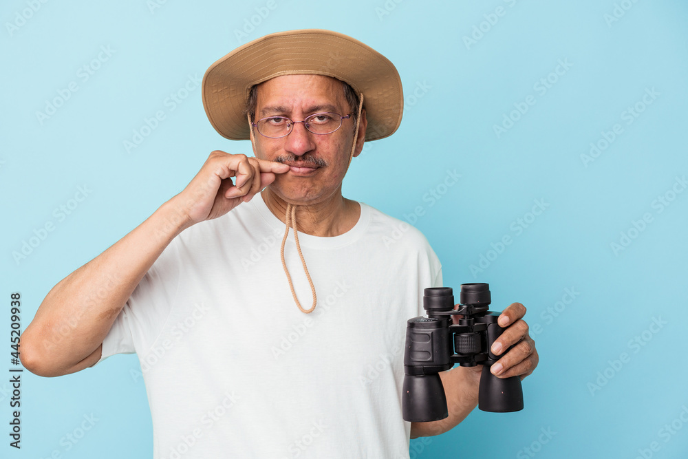 Middle aged indian fisherman holding rod isolated on blue background with fingers on lips keeping a secret. Middle aged indian fisherman holding rod isolated on blue background with fingers on lips keeping a secret.