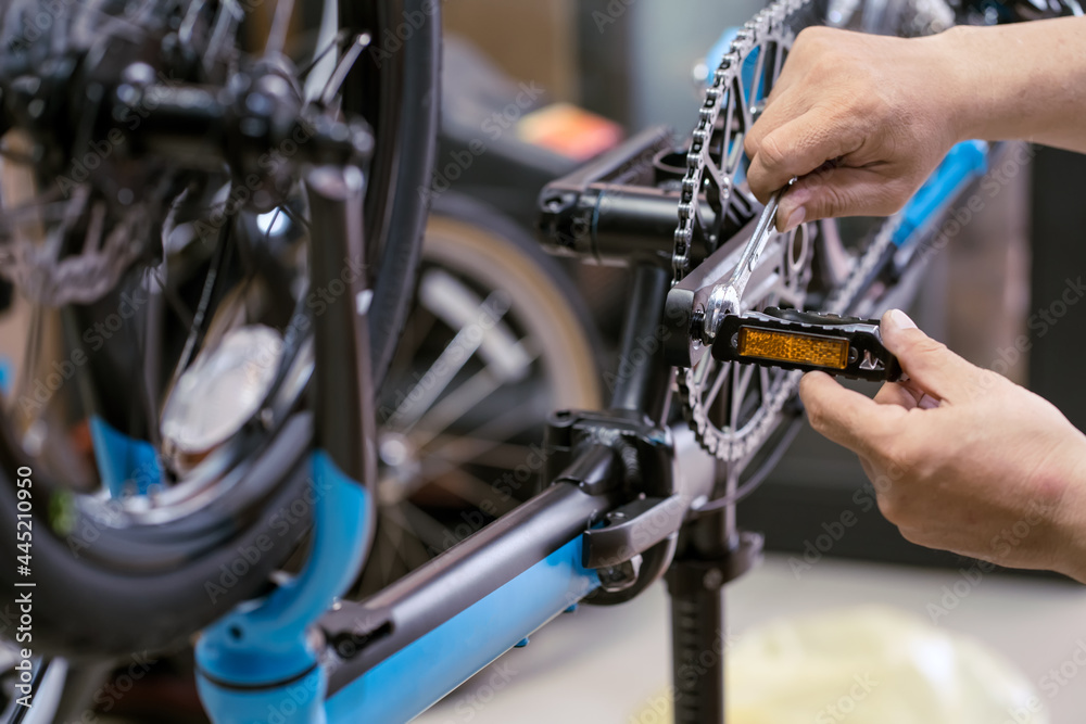 Obraz premium Bike mechanic repairs folding bicycle in Workshop. adjust Bike Pedals . Bicycle Maintenance and Repair concept