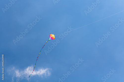 Child's rainbow coloured diamond kite with tail flying high in clear blue summer sky