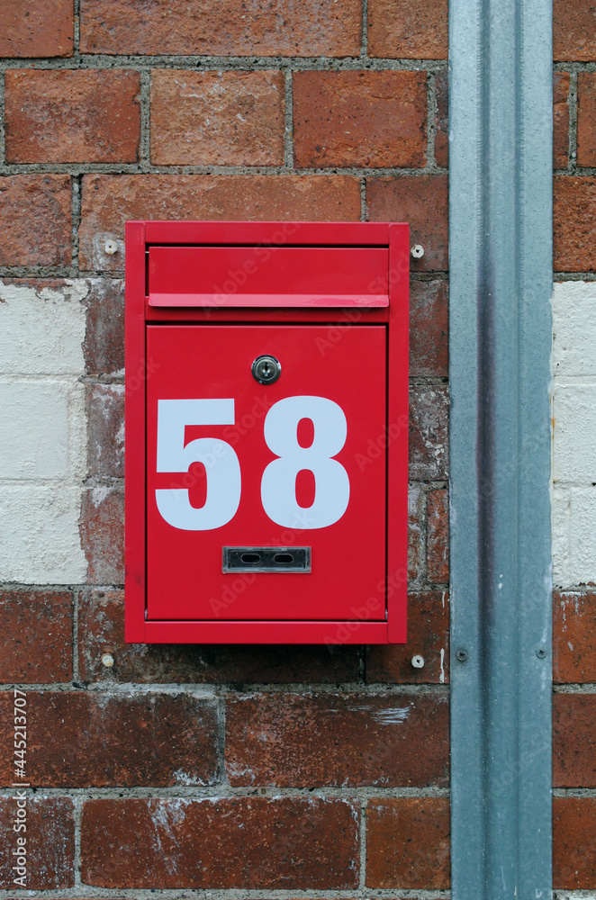 Close Up of Red Metal Mail Box with White Number 58 Attached to Brick Wall 