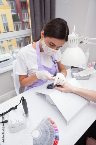 Vertical shot of professional manicurist wearing medical face mask while working