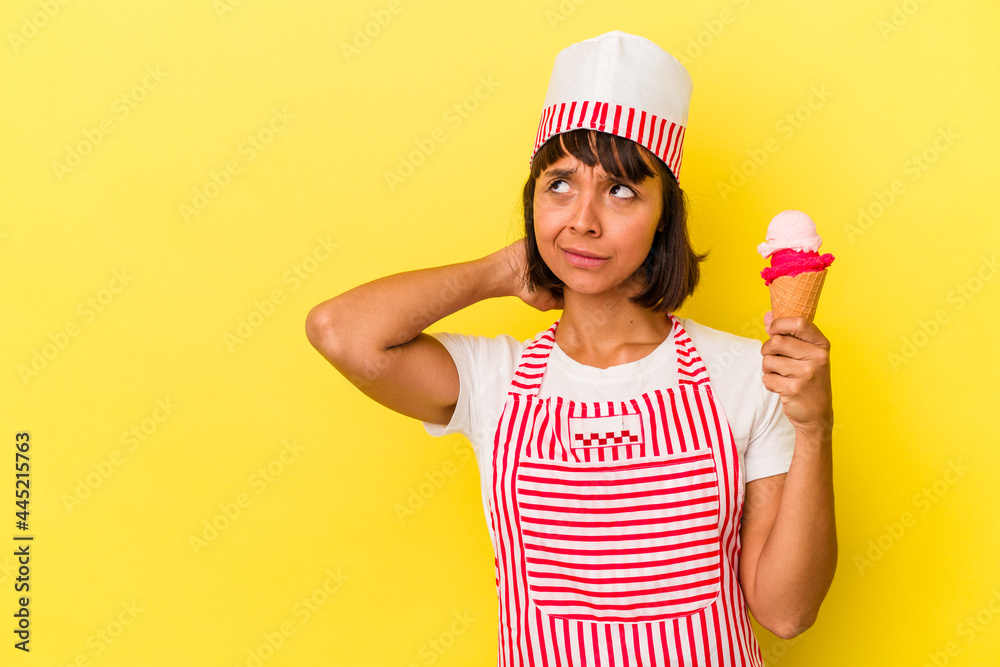 Young mixed race ice cream maker woman holding an ice cream isolated on yellow background touching back of head, thinking and making a choice. Young mixed race ice cream maker woman holding an ice cream isolated on yellow background touching back of head, thinking and making a choice.
