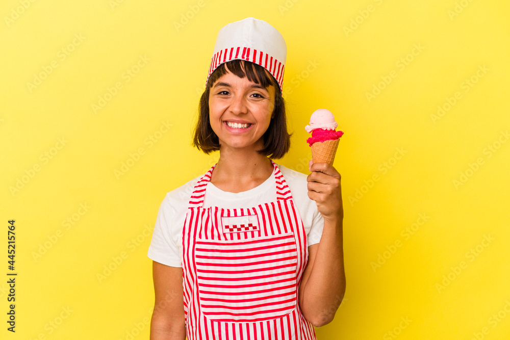 Young mixed race ice cream maker woman holding an ice cream isolated on yellow background happy, smiling and cheerful. Young mixed race ice cream maker woman holding an ice cream isolated on yellow background happy, smiling and cheerful.